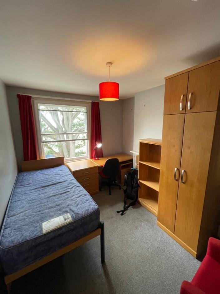 シングルベッドと机、収納棚が並ぶシンプルな学生寮の一人部屋